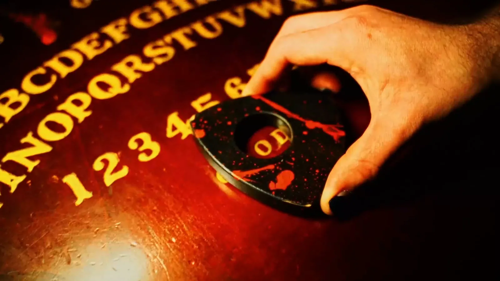 A hand guiding the planchette across a blood-spattered spirit board in The Possession